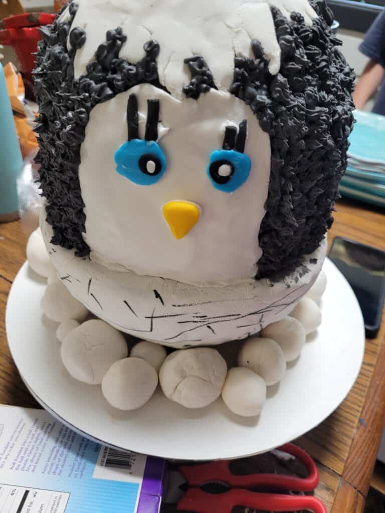 penguin cake, chick hatching out of an egg, white fondant on egg and penguin face, black icing for skin, blue eyes, yellow beak