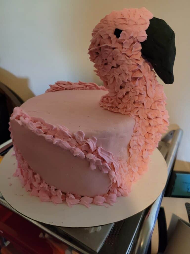 Flamingo cake, round cake with neck and head of a flamingo attached. pink fondant body with a black fondant beak and eyes. pink icing use to make feather texture