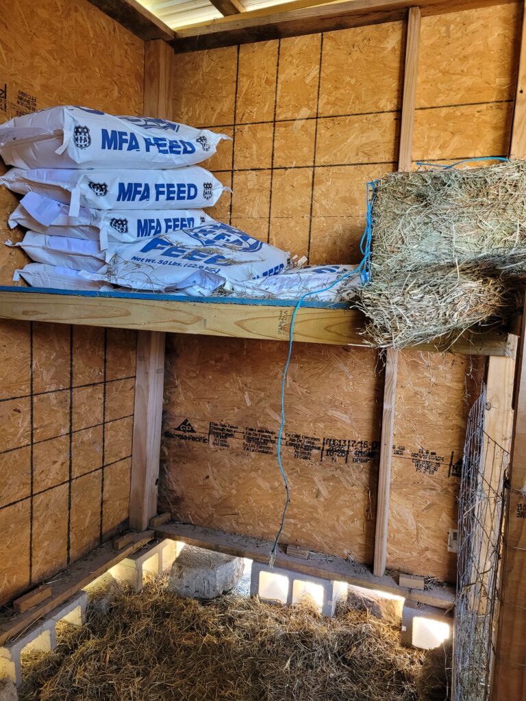 goat barn stall with hay loft, the loft has several feed bags stacked on it and a bale of hay