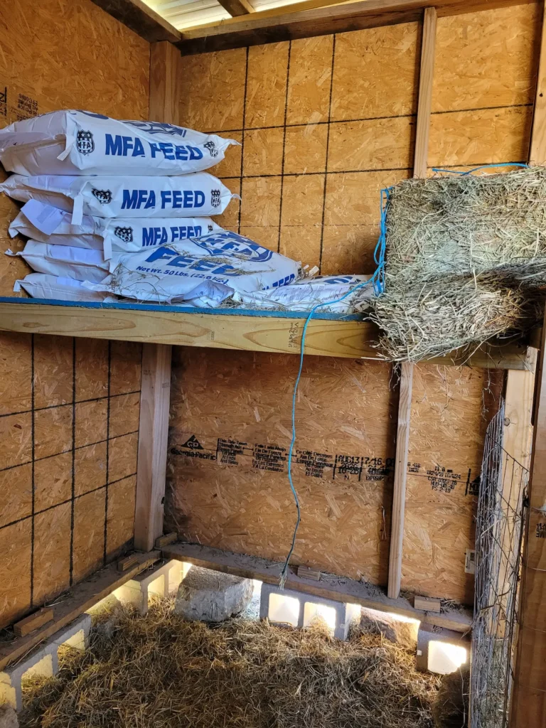 A hay loft, holding several bags of feed and a hay bale inside a stall of a goat barn